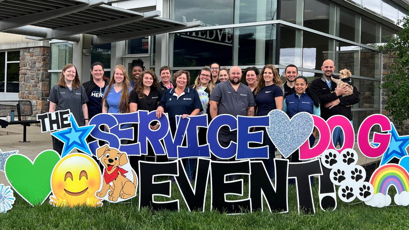 Service Dog Event Cincinnati MedVet Cincinnati team members standing behind large yard sign that says, “The Service Dog Event!” out in front of veterinary hospital